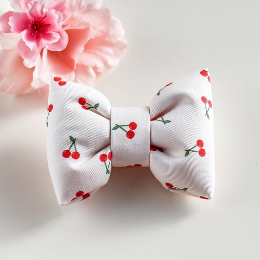 White bow with red cherry pattern and pink flower on a light gray background