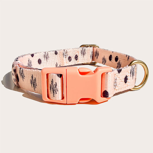 A pink peach dog collar with a black ikat abstract pattern, featuring a bright coral orange plastic buckle and a gold-tone metal ring, shown on a light beige background.