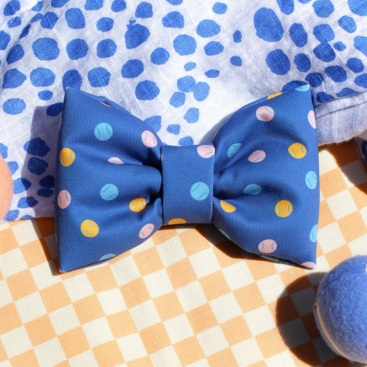 Blue polka dot bow tie on a checkered surface with a patterned shirt.