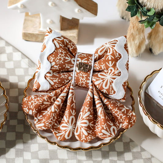 Gingerbread a cotton dog sailor bows with ric rac. Scallop details for tails. Decorative bow with brown and white pattern on a checkered tablecloth. Bop Pop Pets dog bows. Premium elevated handmade dog goods