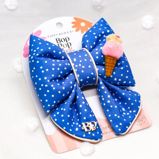 Blue polka dot hair bow with pink ice cream cone on a white background