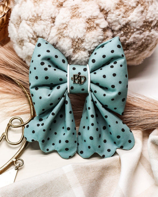 Teal polka dot bow with gold clasp on a neutral background