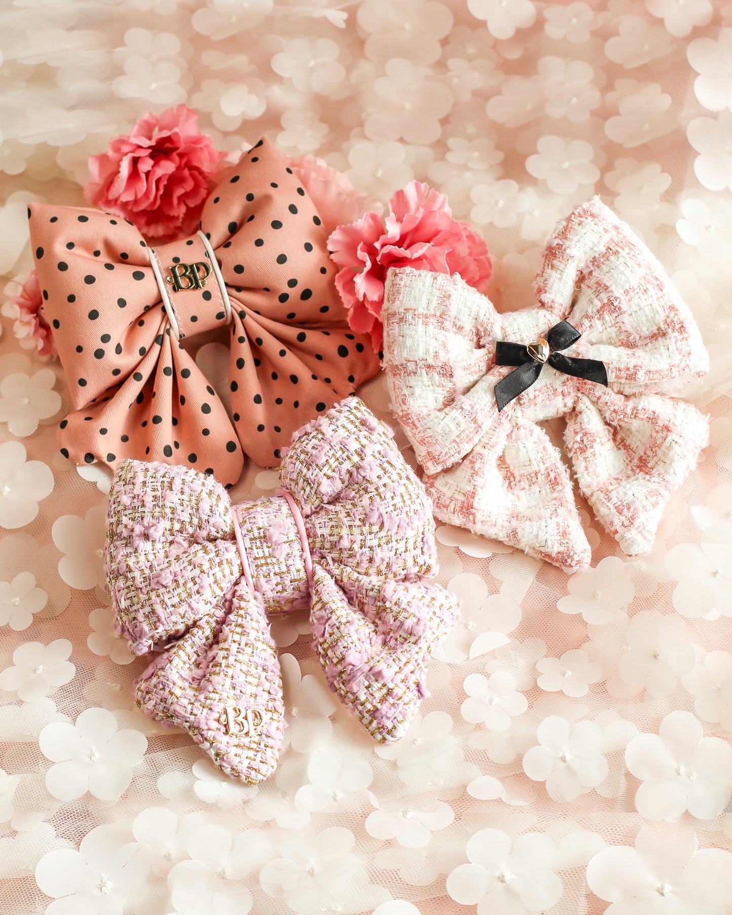 Three decorative bows with flowers on a soft pink background. Polka dot and pink lilac tweed sailor bow for dogs cats in a textured tweed with gold threading. Bop Pop pets pet accessory.