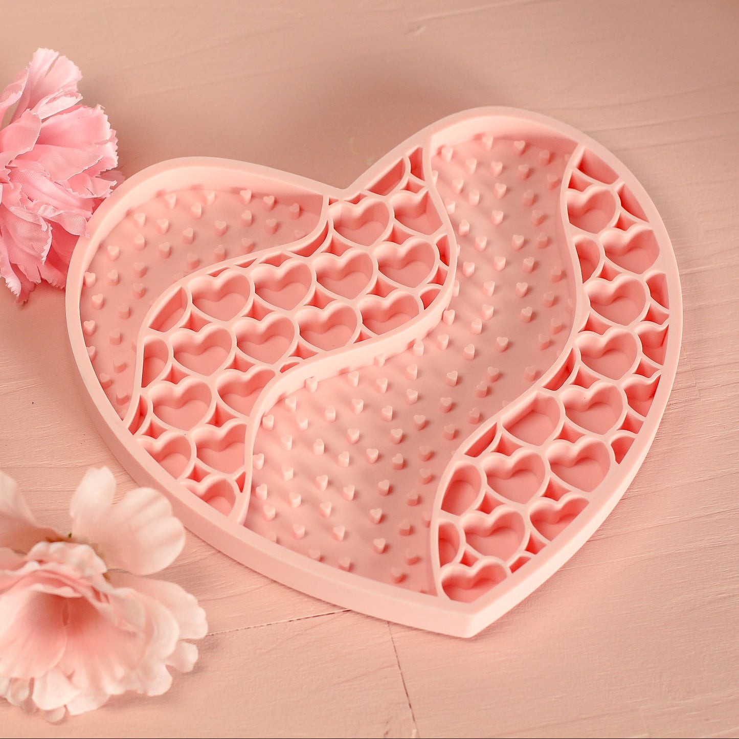 Heart-shaped pink silicone mold on a wooden surface with pink flowers.