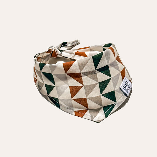 A fabric pet bandana with a geometric triangle pattern in rust orange, dark green, and cream, featuring a small white brand tag that reads 'BOP POP'.