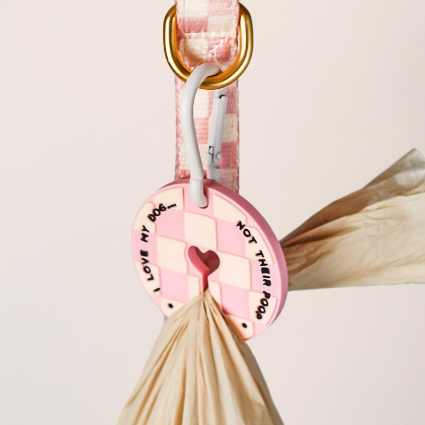 Pink dog leash with checkered pattern and decorative tags on a light gray background