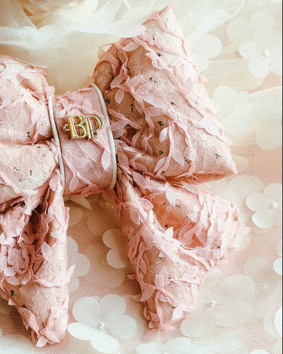 Pink lace bow with a gold emblem on a floral fabric background