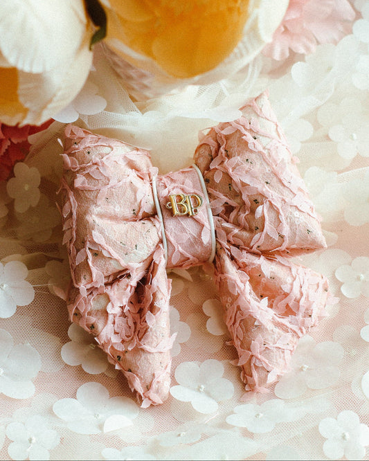 Pink lace bow with a gold emblem on a floral fabric background