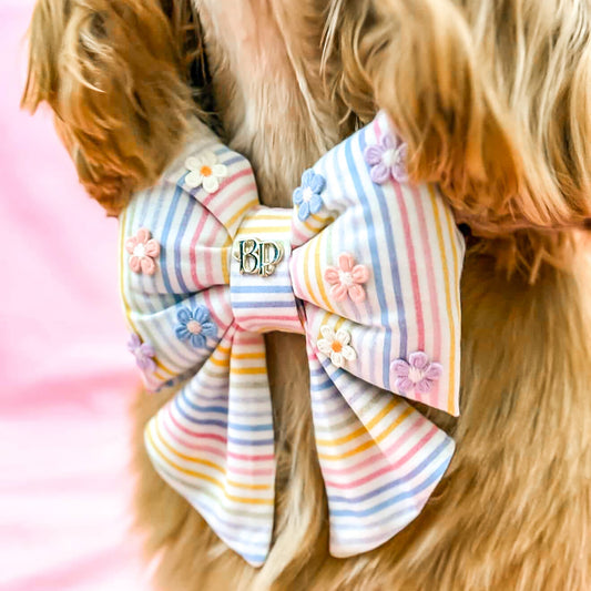 Dog wearing a colorful striped bow with floral details on a blurred pink background