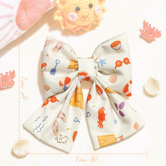 Colorful dog bow with ocean-themed design on a textured surface. Bop Pop Pets for trendy dogs and cats. Size dimensions 7in x 7in