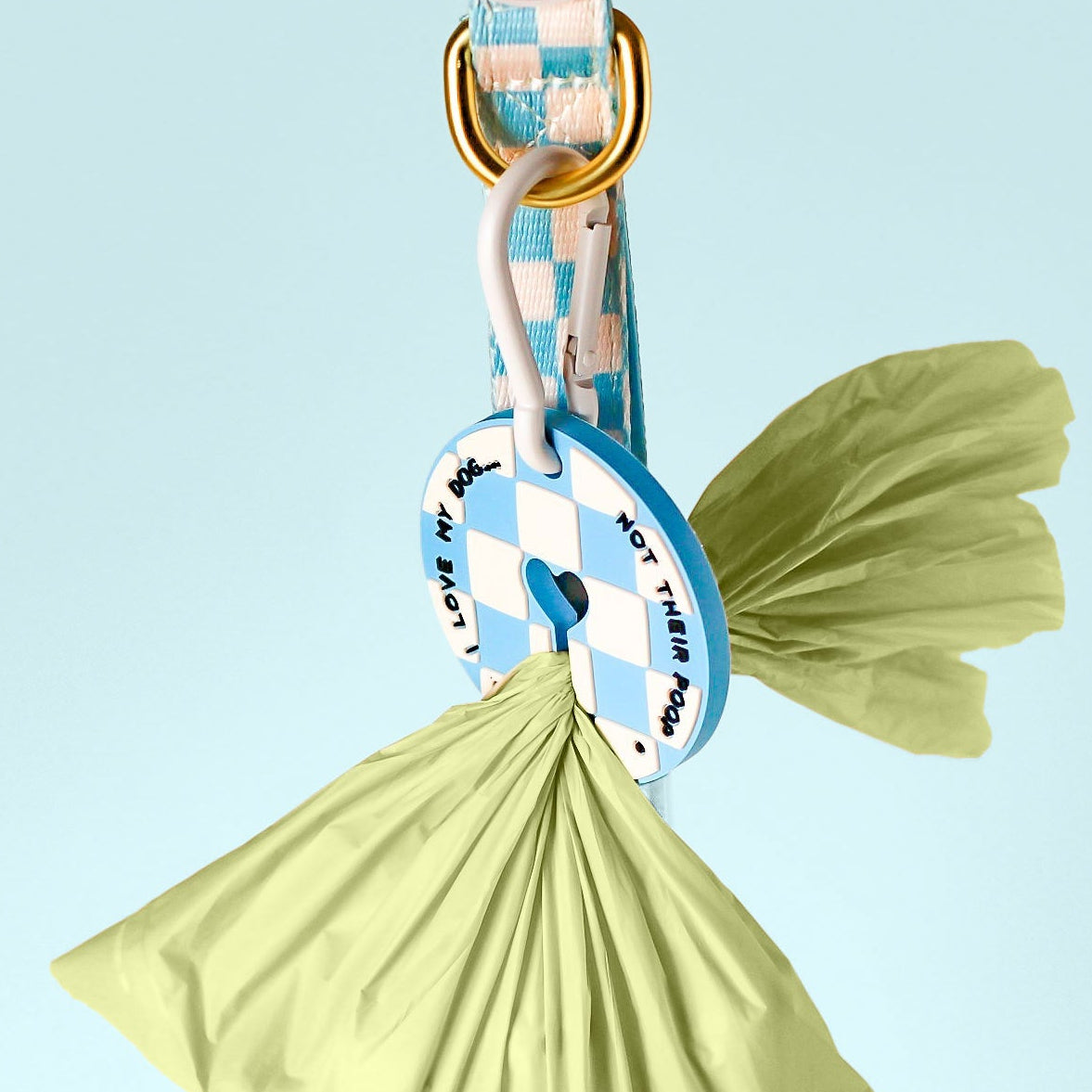 A pet leash with a blue and white checkered pattern, gold metal hardware, and a matching round tag, shown with two light green plastic bags hanging from the ring against a light blue gradient background.
