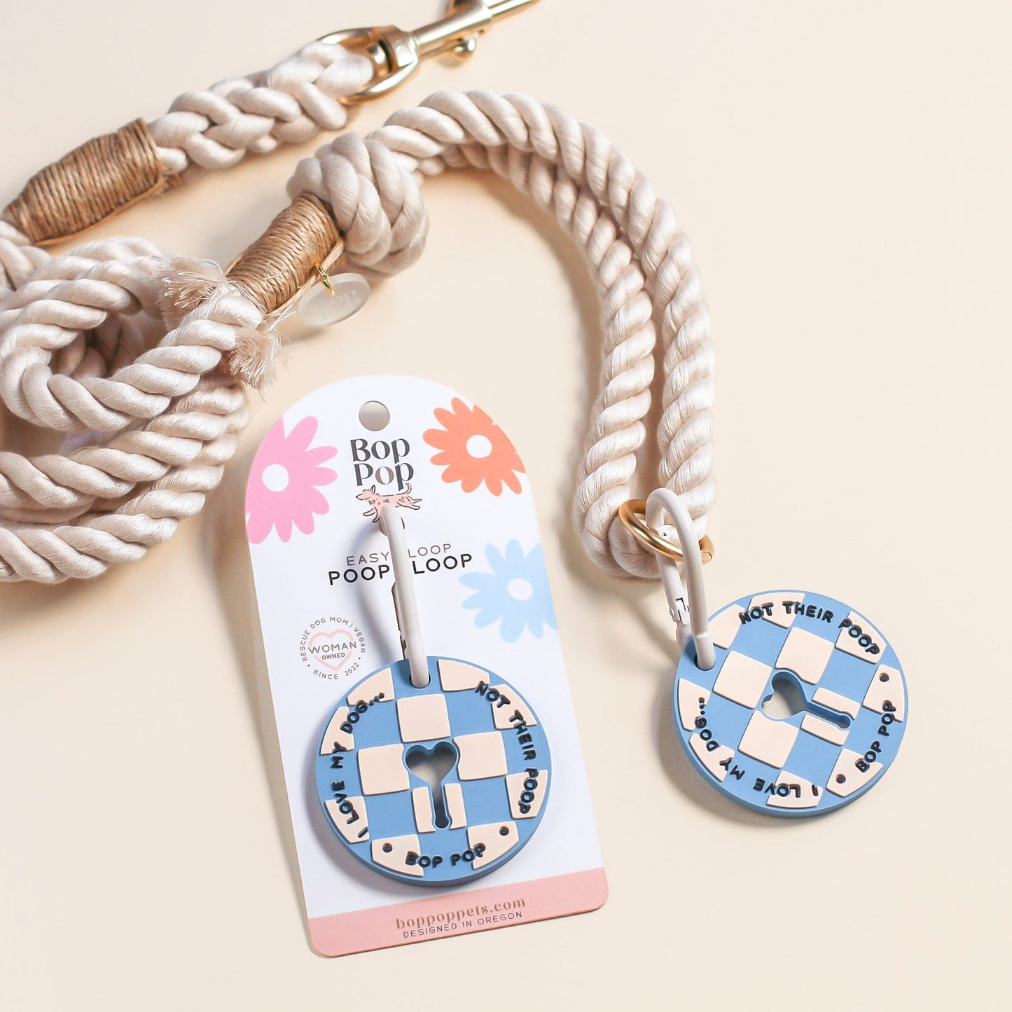A rope dog leash with a round blue-and-white checkered poop loop attachment, shown with its retail card on a light beige background.