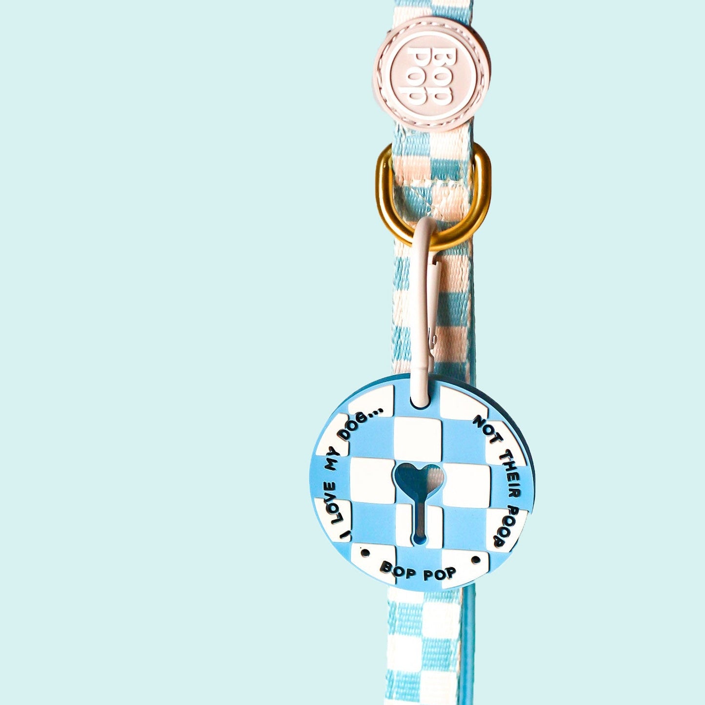 A light blue and white checkered dog collar with a round metal ID tag featuring a blue heart-shaped keyhole in the center and the text 'I LOVE MY DOG.
