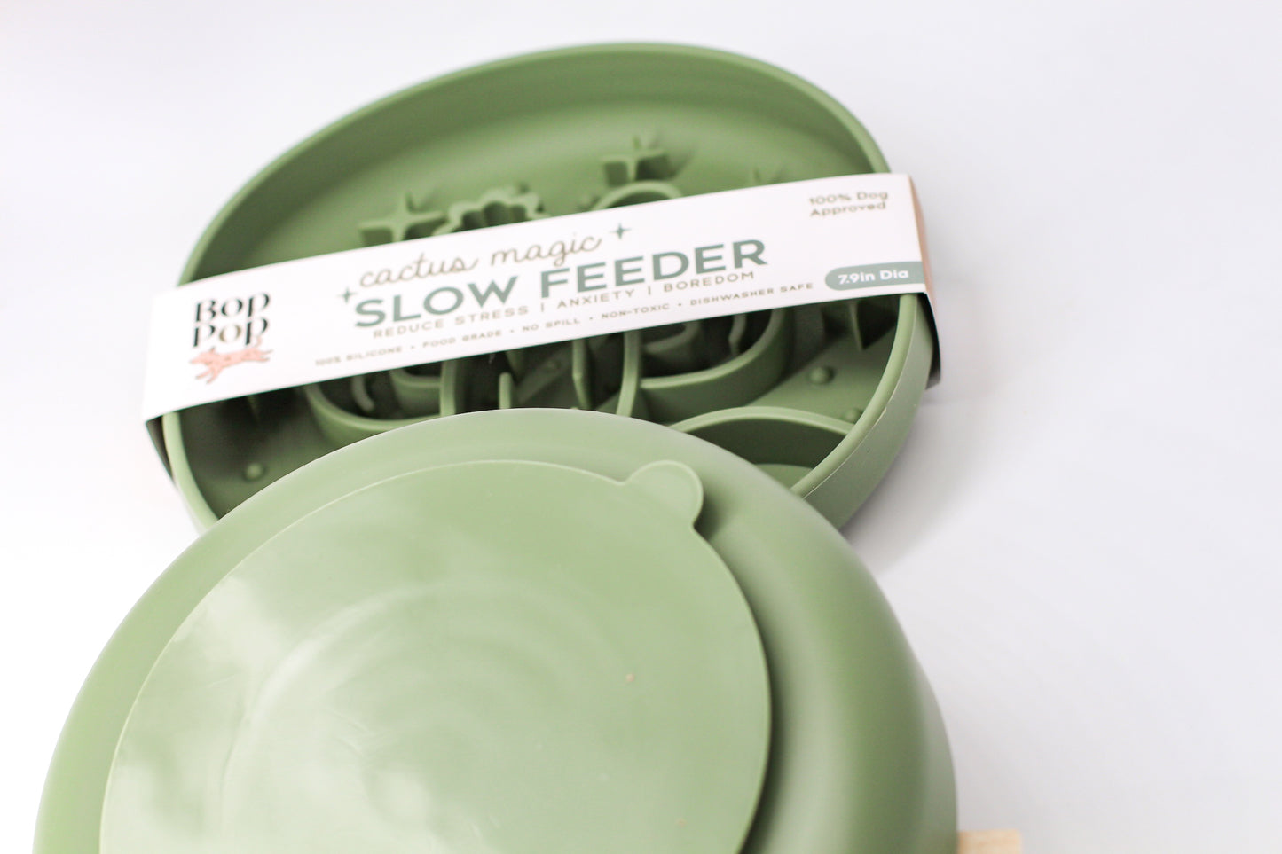 Cactus Magic Slow Feeder staggered on white background with upper feeder displaying blurred view of brand packaging labeled 'Cactus Magic SLOW FEEDER' and lower feeder displaying backside of smaller circle suction pad with a small half-circle tab on edge.