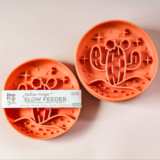 Cactus Magic Slow Feeder staggered on blush white background with lower left feeder displayed with brand packaging labeled 'Cactus Magic SLOW FEEDER' and upper right feeder displaying 3 dimensional pattern of a cactus with blooming flower in the desert hill with 5 stars.