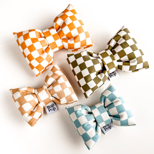 Four checkered hair bows in orange, green, and blue on a white background