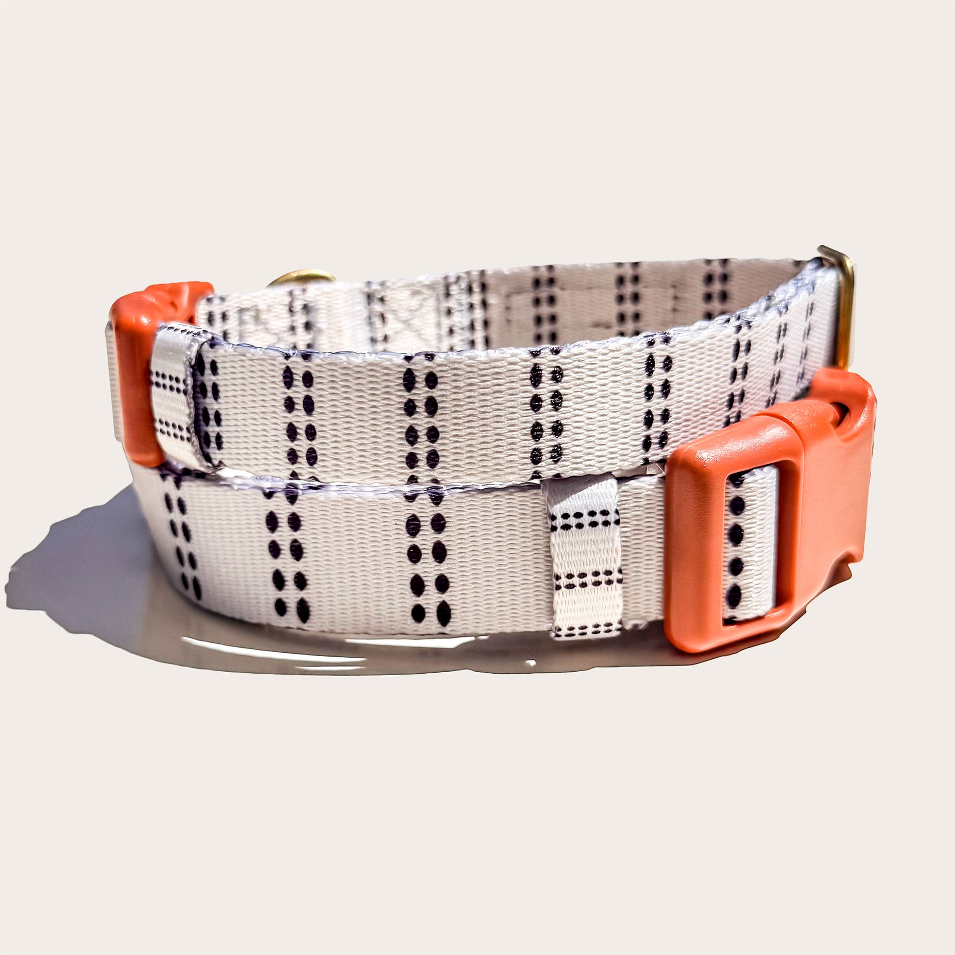 A modern farmhouse styled dog collar with a white base, black dotted vertical stripe pattern, and bright orange plastic buckle and keeper, shown on a light beige background.