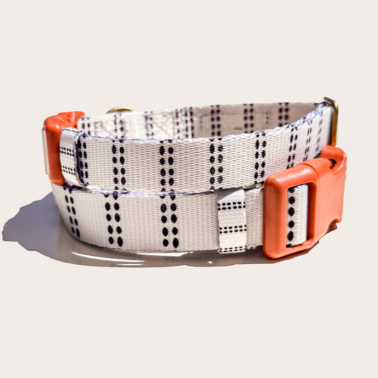 A modern farmhouse styled dog collar with a white base, black dotted vertical stripe pattern, and bright orange plastic buckle and keeper, shown on a light beige background.