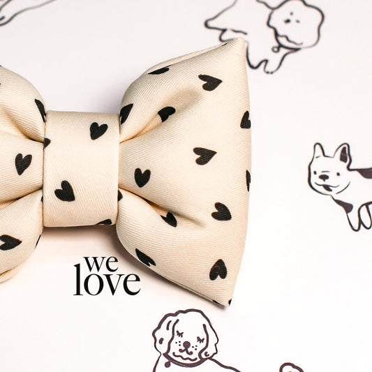 Cream-colored bow tie with black heart patterns on a white background with dog illustrations.