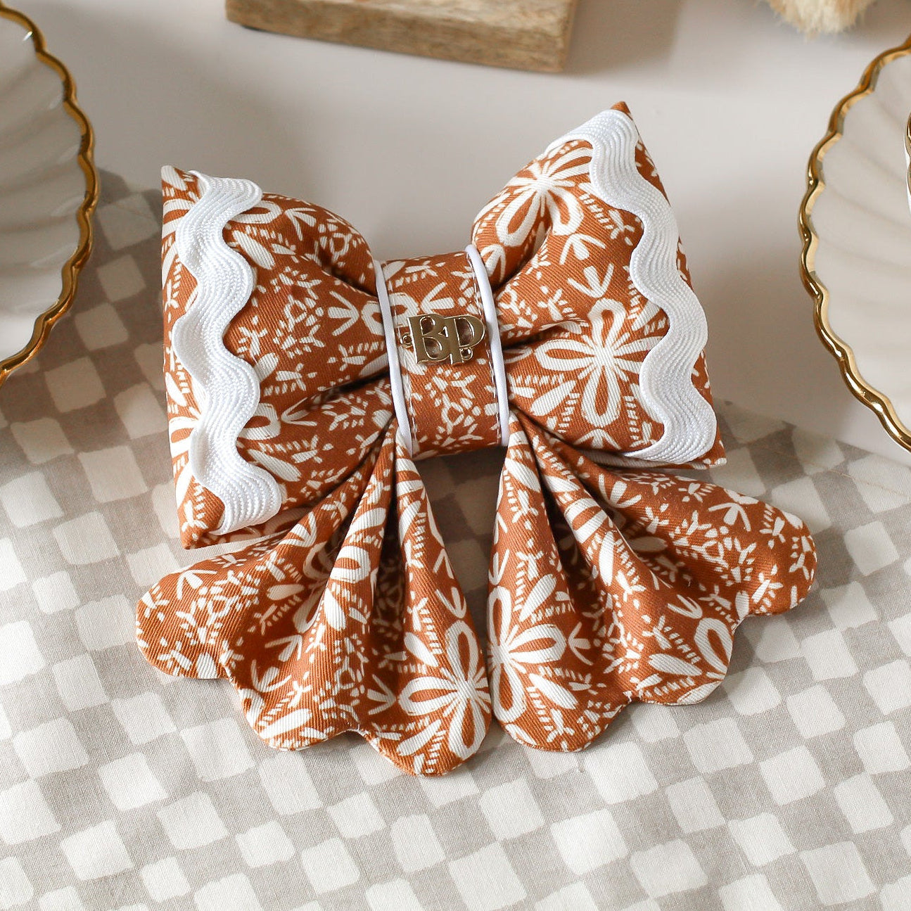 Gingerbread a cotton dog sailor bows with ric rac. Scallop details for tails. Decorative bow with brown and white pattern on a checkered tablecloth. Bop Pop Pets dog bows. Premium elevated handmade dog goods