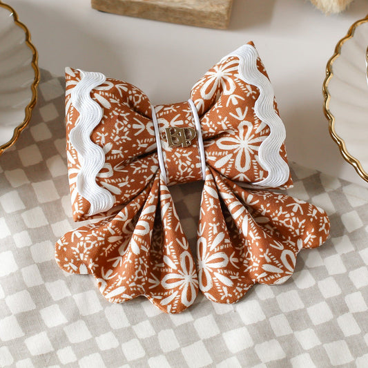 Gingerbread a cotton dog sailor bows with ric rac. Scallop details for tails. Decorative bow with brown and white pattern on a checkered tablecloth. Bop Pop Pets dog bows. Premium elevated handmade dog goods
