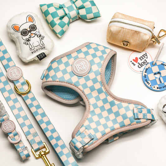 Blue checerkboard pet accessories including a harness, collar, and poop loop with checkered pattern on a white background