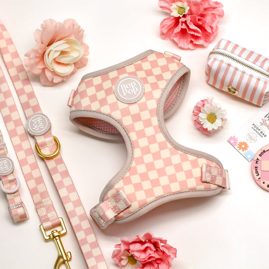 Pink checkered dog harness with matching leash, collar, and accessories on a white background with flowers.