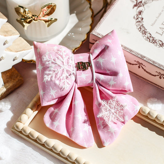 Decorative pink bow with snowflake patterns on a cookie, with a box labeled Lauduree Paris. Holiday dog bows from premium handmade dog goods. Bop Pop Pets scalloped bows. Festive modern style