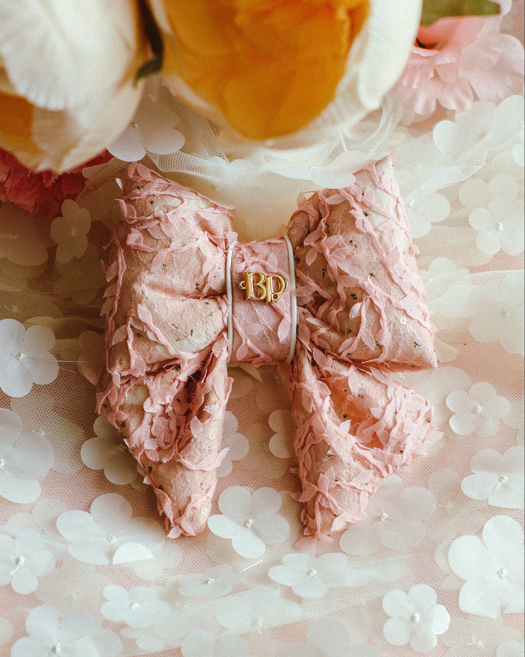 Pink hair bow with gold letter 'B' on a floral background