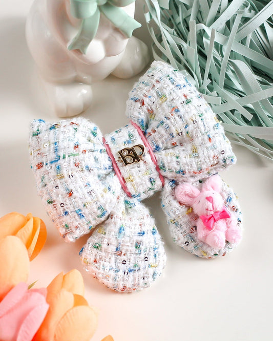 Crocheted baby booties with colorful pattern on a white surface with Easter decorations.