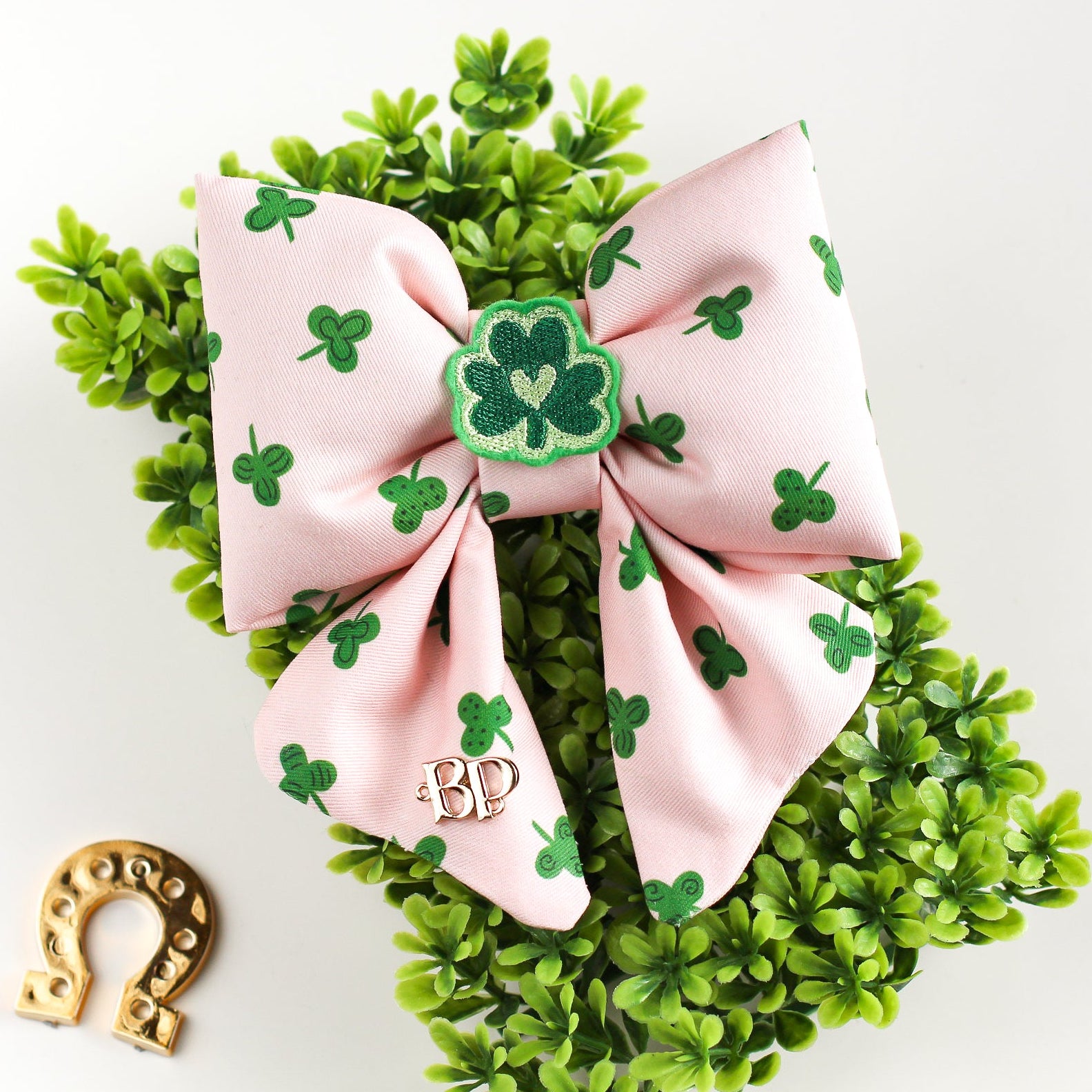 Pink bow with shamrock design on a green wreath with a gold horseshoe on a white background