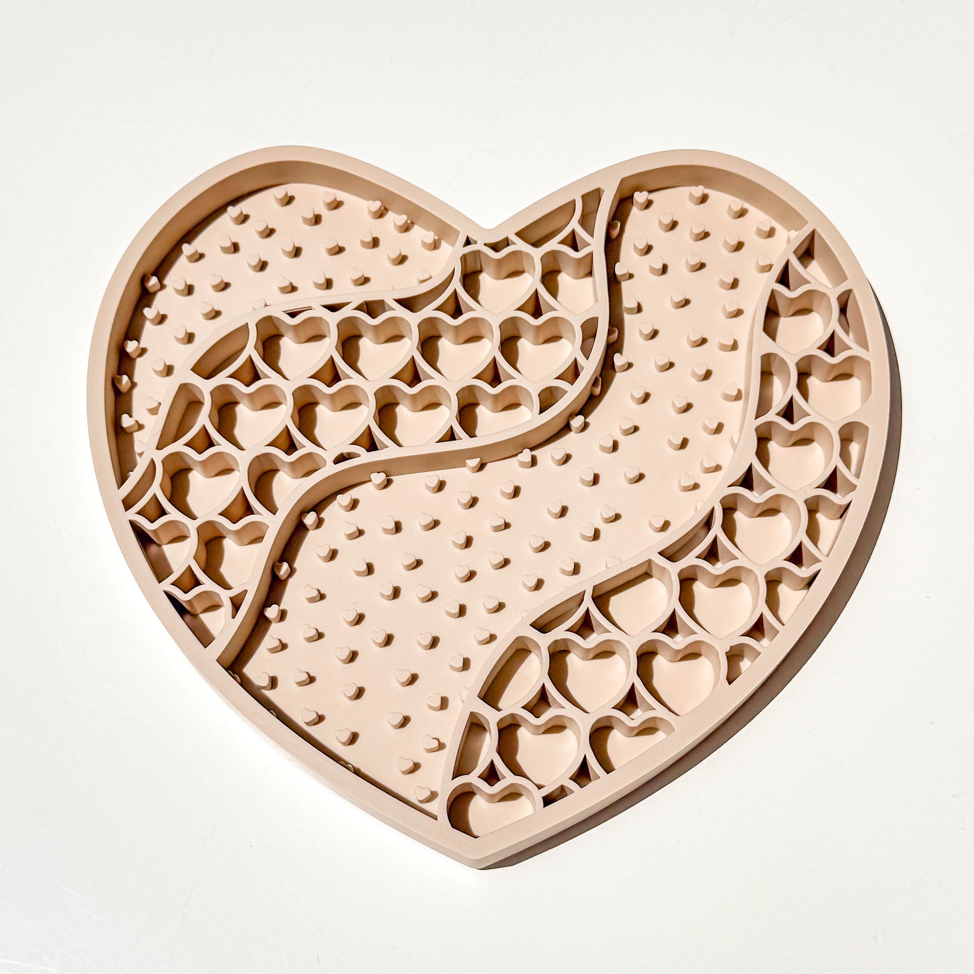 A heart-shaped silicone food-grade puzzle pet lickmat featuring textured raised patterns and heart-shaped cutouts, and wavy pattern of hearts and dots shown on a plain white background.