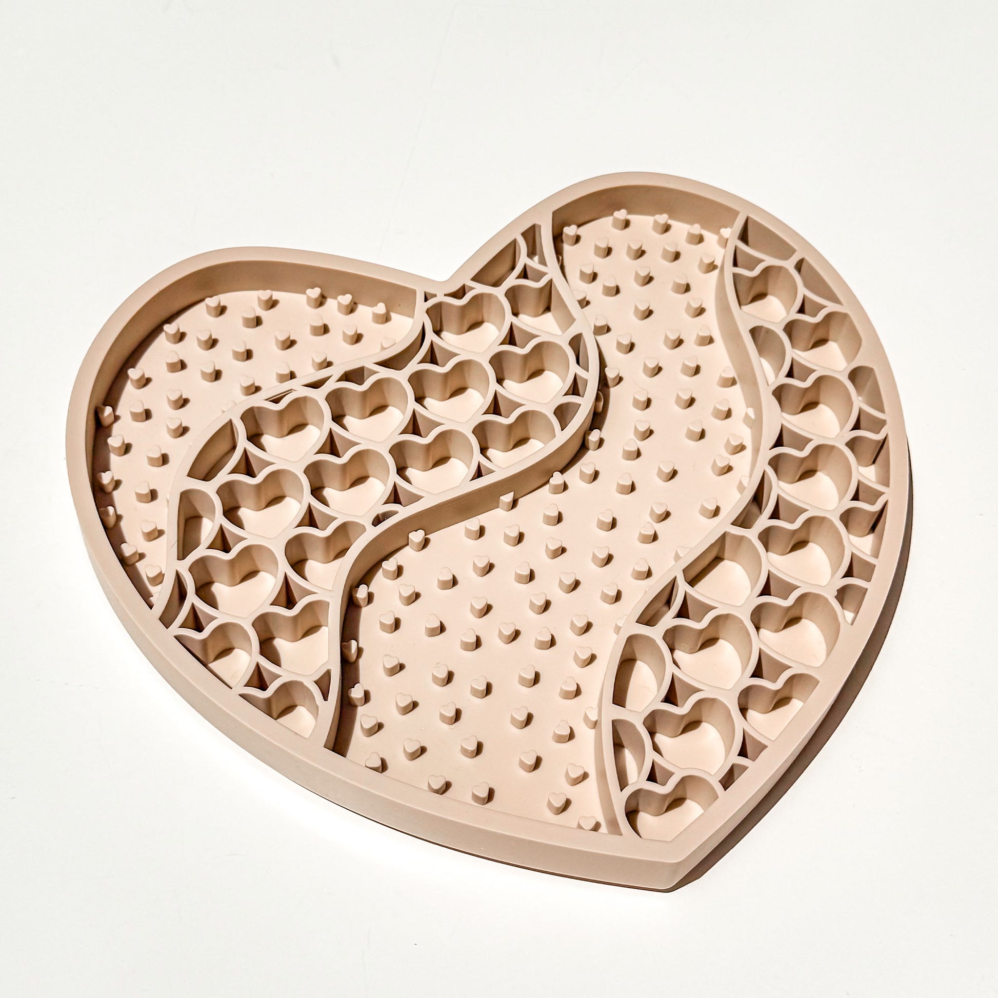 A heart-shaped beige silicone pet lick mat with textured bumps and cutout heart patterns, shown on a clean white background.