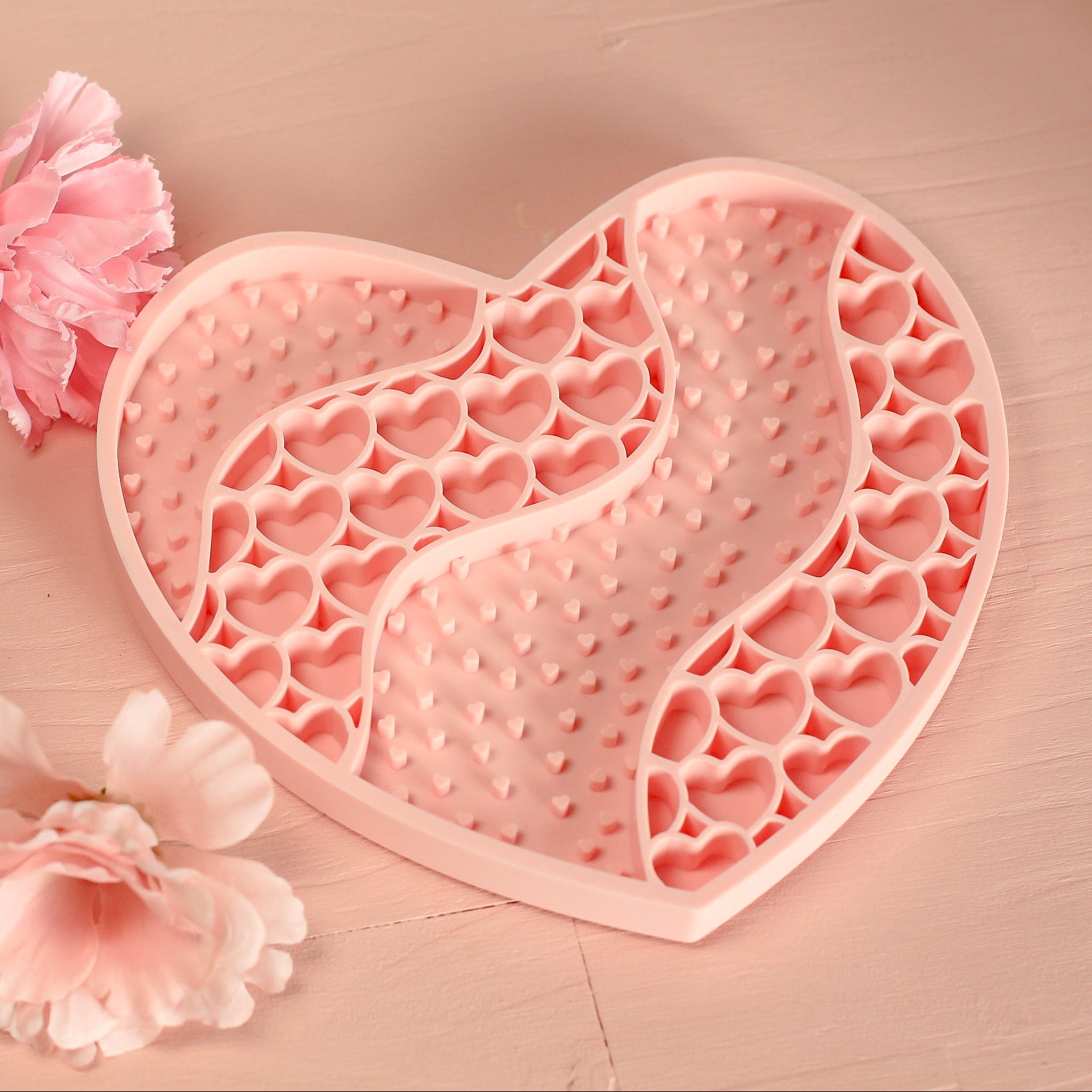 Heart-shaped pink silicone mold on a wooden surface with pink flowers.