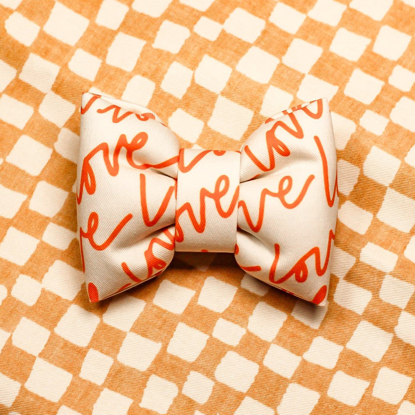 Love Text White bow tie with orange text on a checkered orange and white background. Bop Pop Pets accessories
