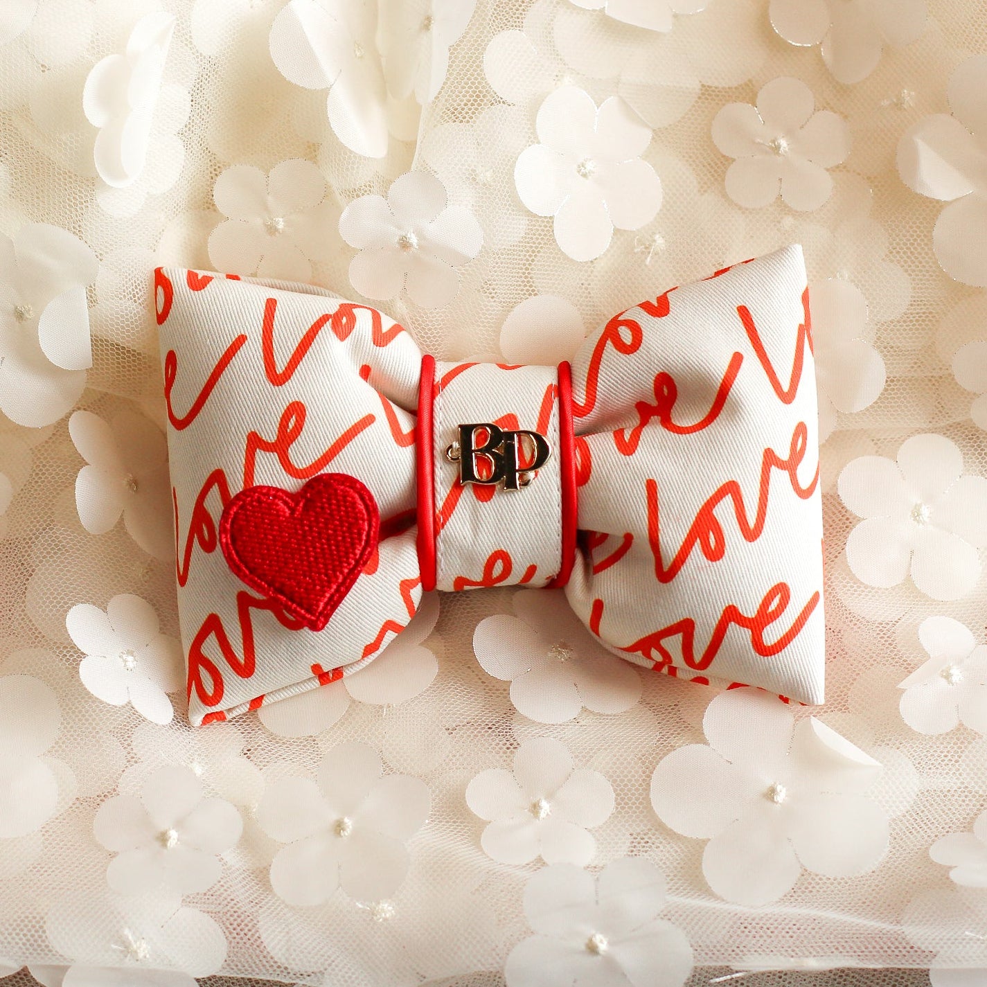 Bow tie with red heart and red text on a white fabric background