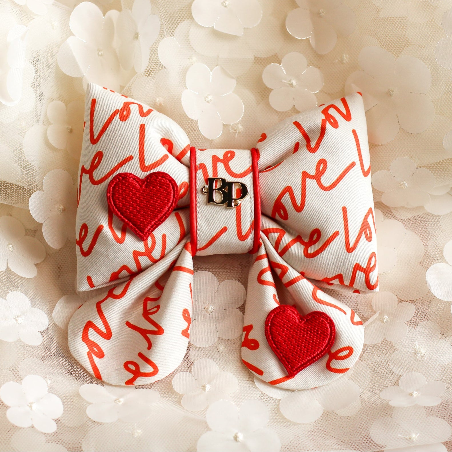 White bow with red hearts and 'Love' text on a soft, blurred floral background
