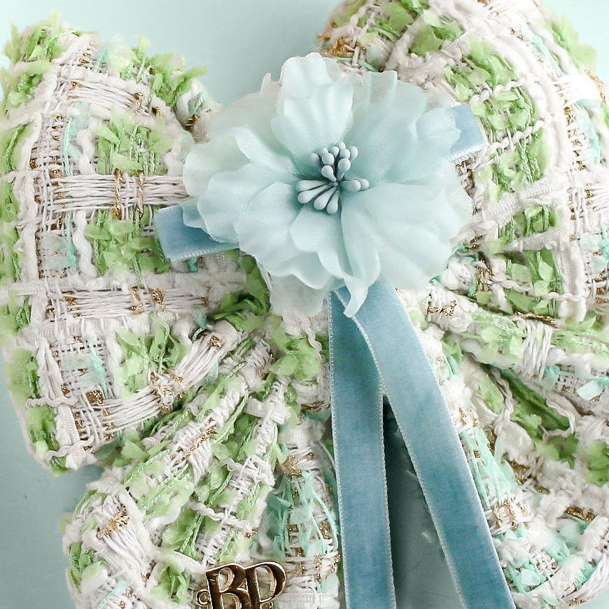 Decorative heart-shaped object with a ribbon and flower on a light blue background