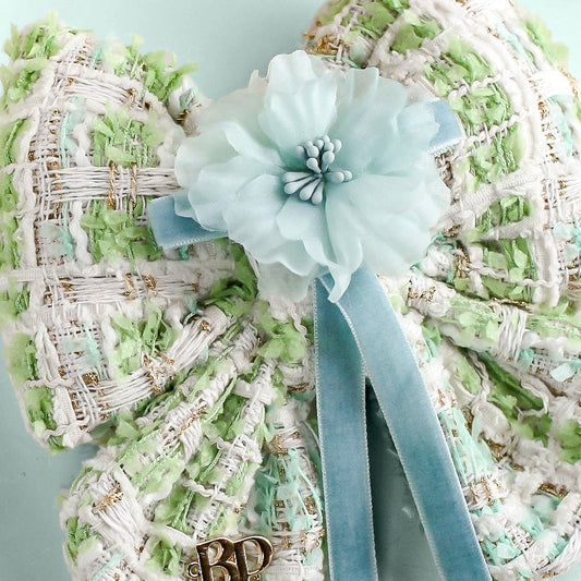 Decorative heart-shaped object with a ribbon and flower on a light blue background