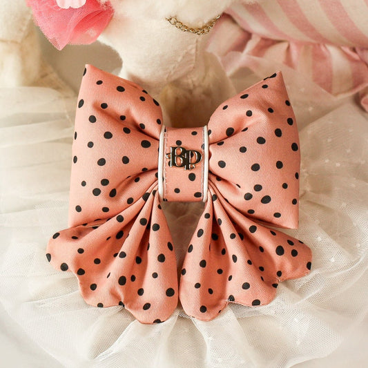 Poodle doll with a pink pet bow in black dots and flowers on a white cushion