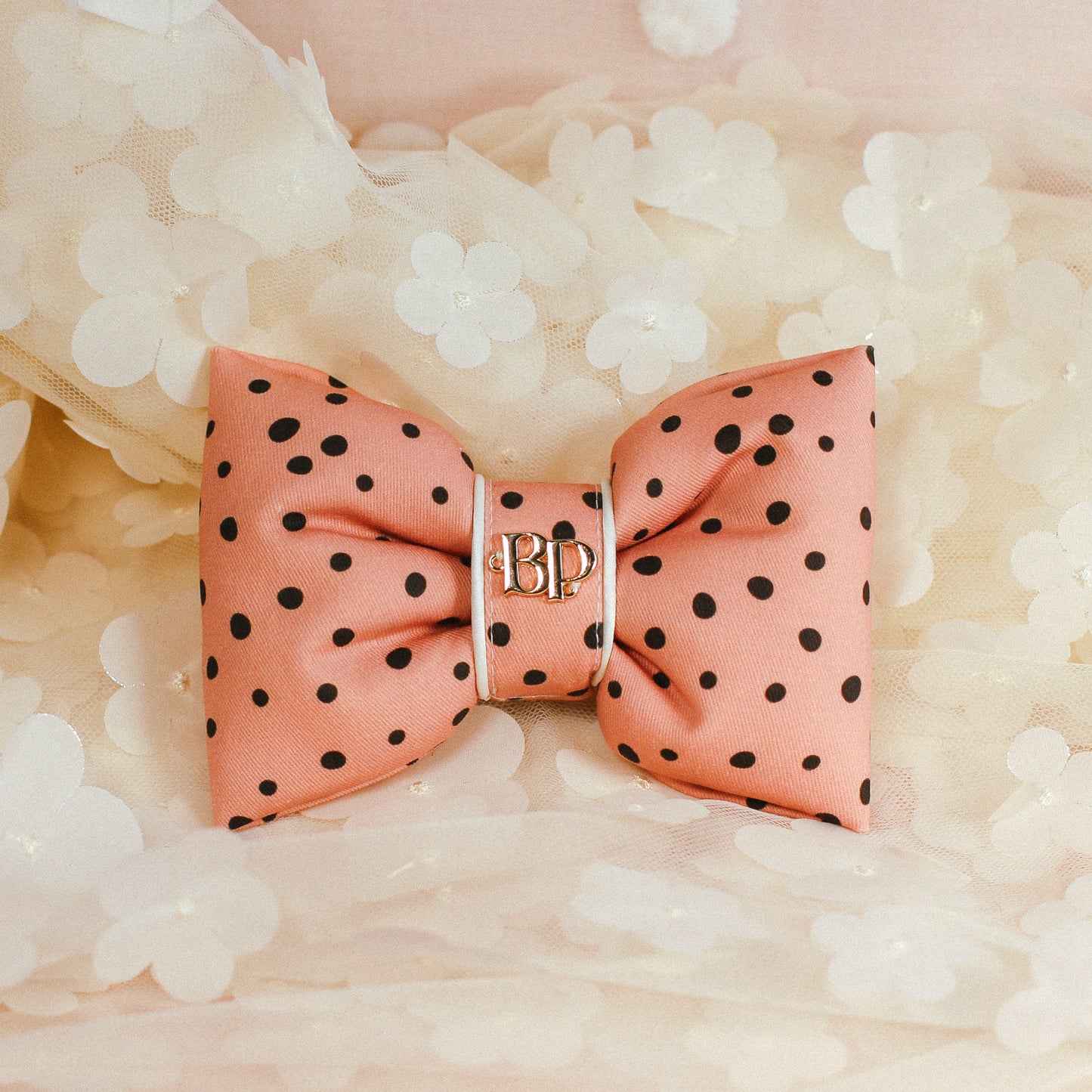 Pink polka dot bow with gold logo on a soft white background