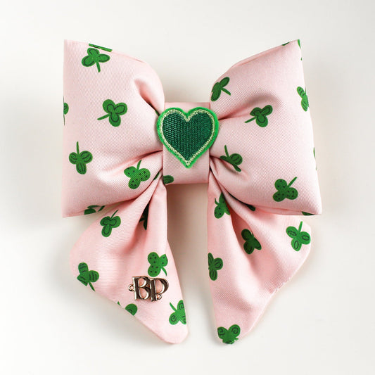 Pink hair bow with green shamrock pattern and heart design on a white background
