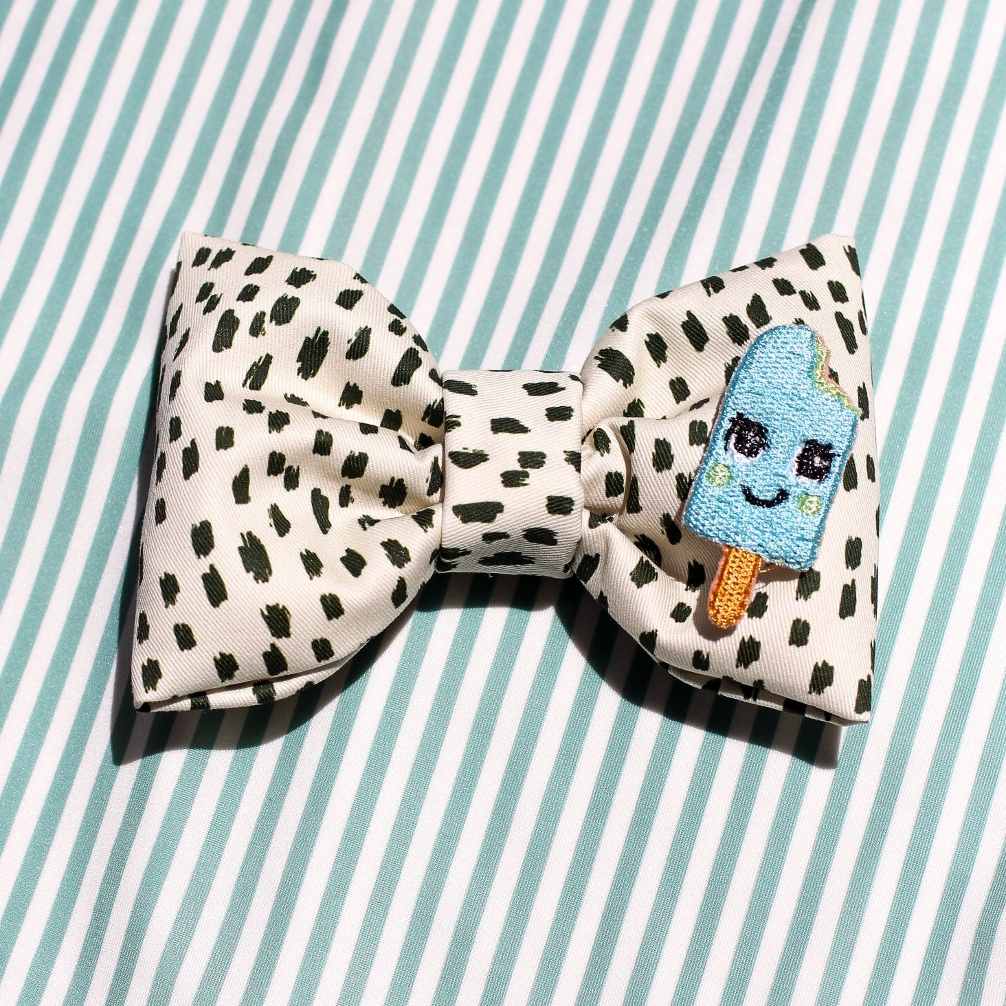 icy pop aqua blue bow tie in black dotted cotton fabric over mint green stripes background. Modern trendy bows for pets dogs and cats by Bop Pop Pets
