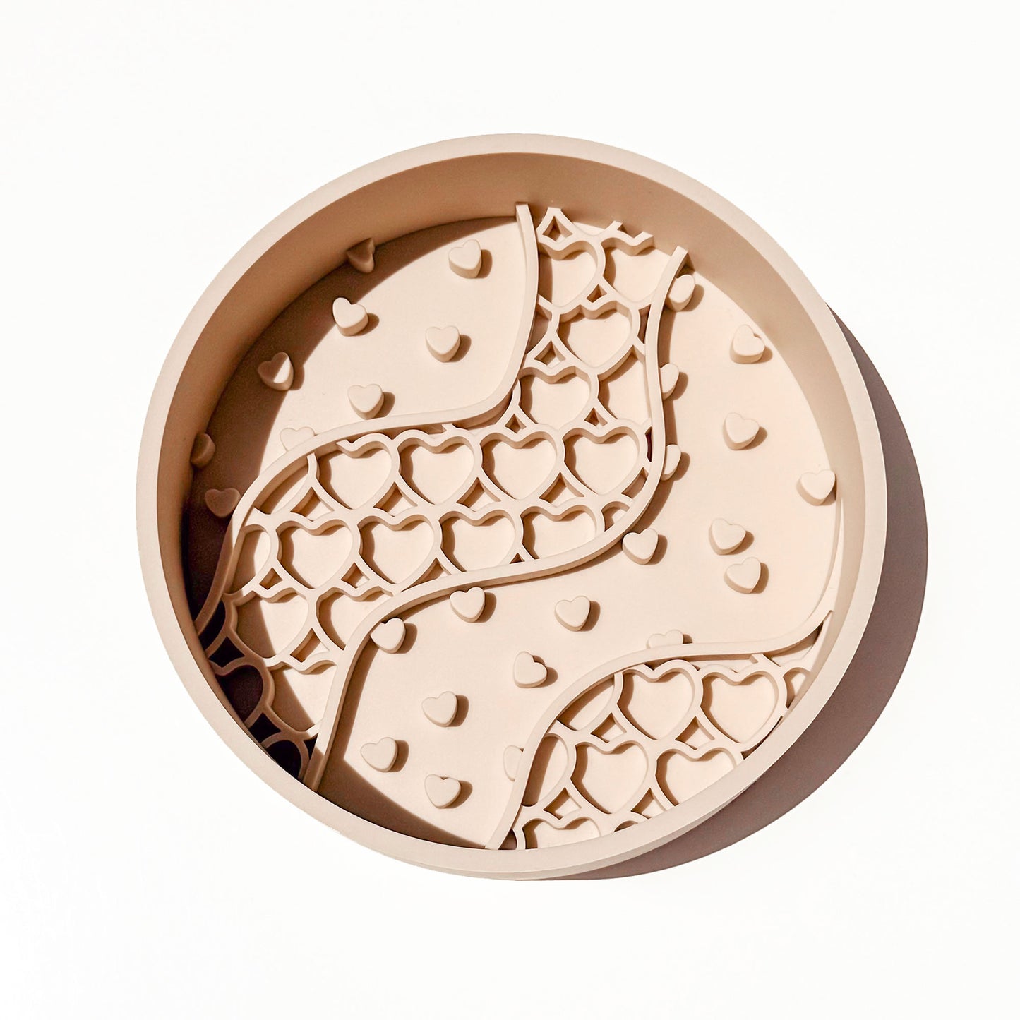 A round beige silicone pet slow feeder bowl with a raised wavy pattern of hearts, photographed from directly above on a clean white background.