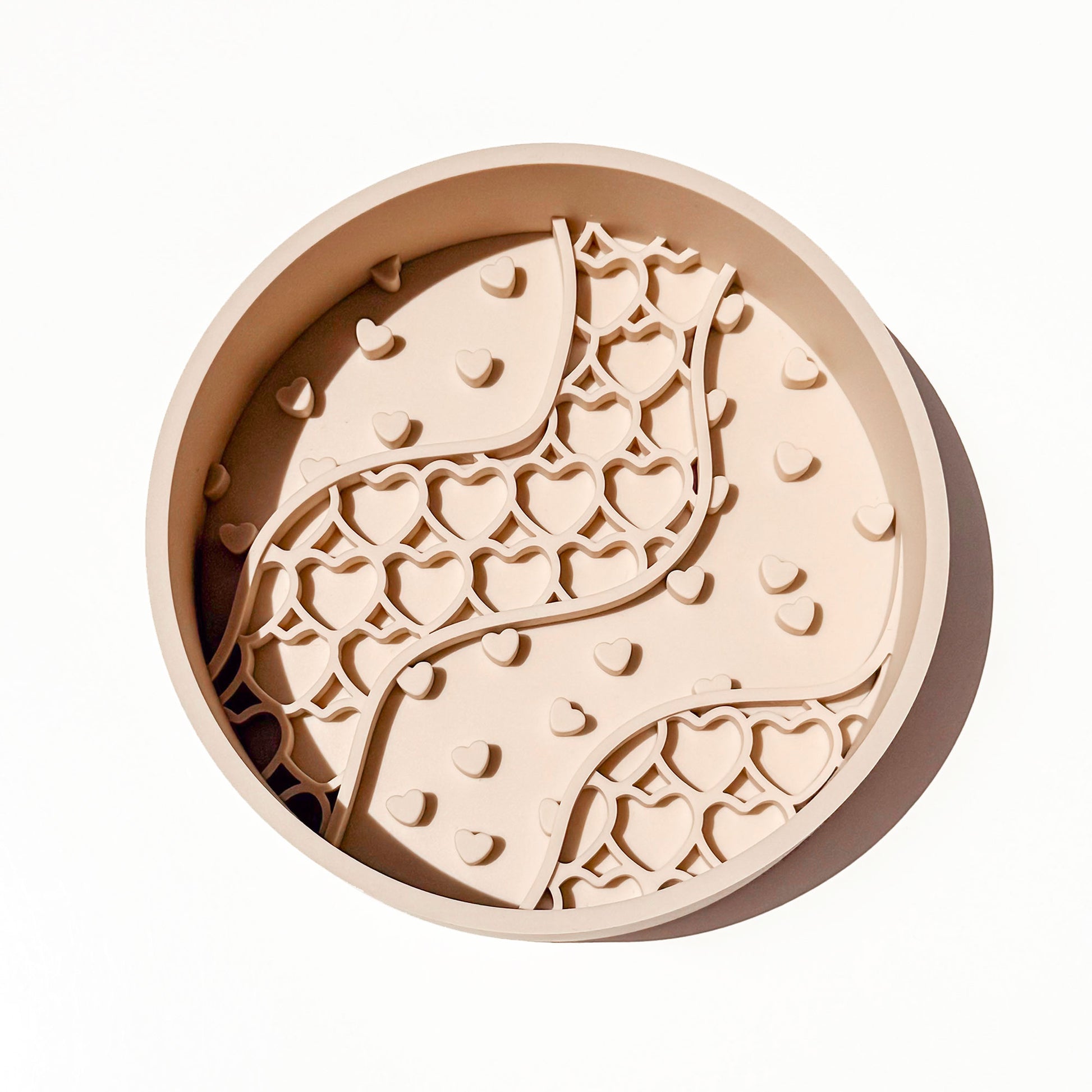 A round beige silicone pet slow feeder bowl with a raised wavy pattern of hearts, photographed from directly above on a clean white background.