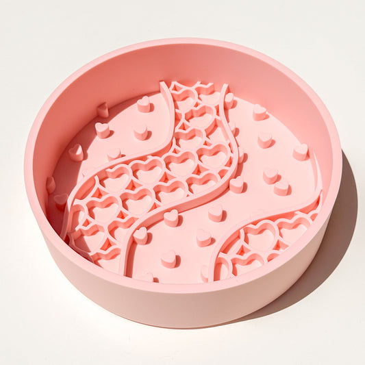 A round pink blush colored silicone pet slow feeder bowl with a wavy channel pattern and heart-shaped cutouts, shown on a clean white background with a soft shadow.