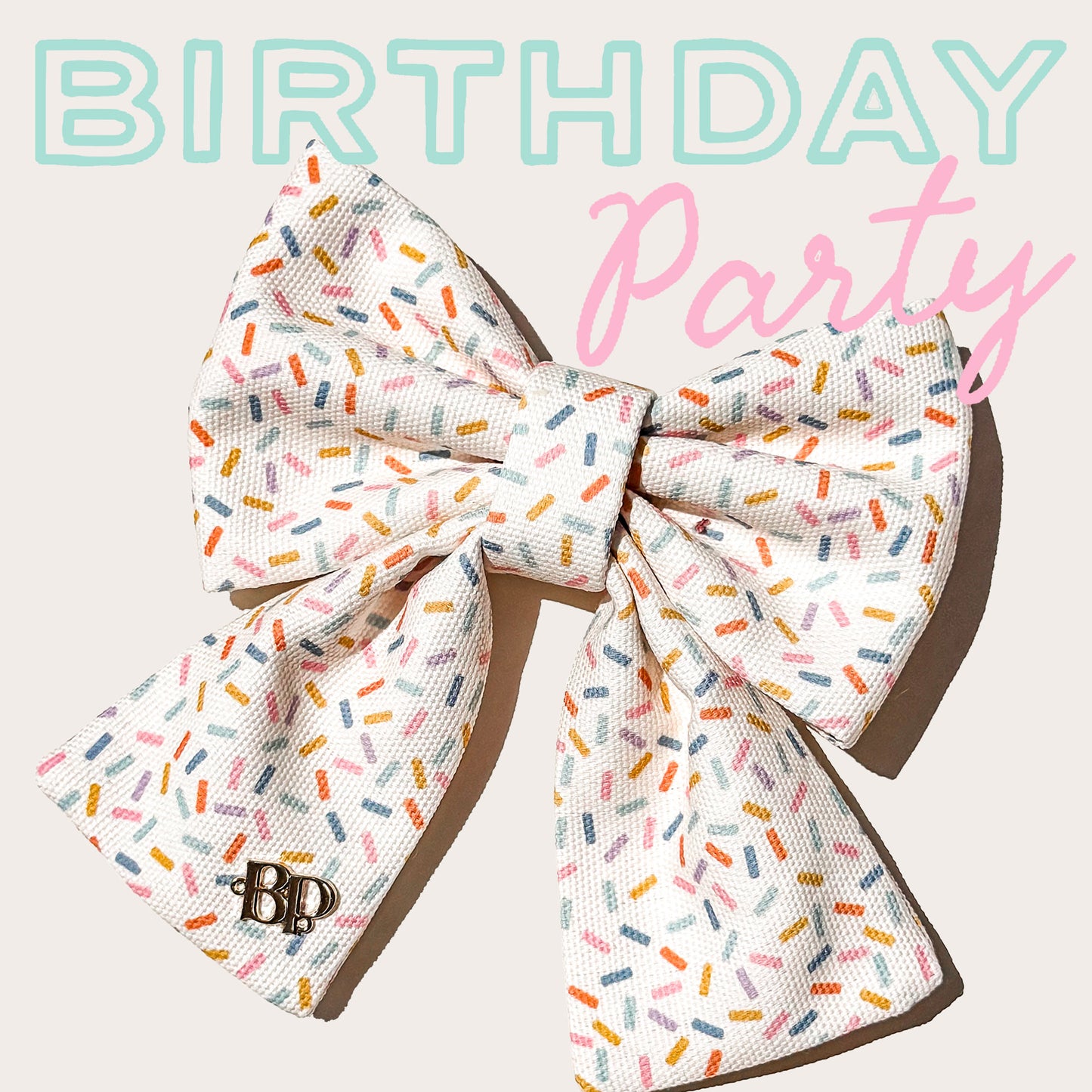 A large pet bow with a white base and a colorful sprinkle pattern, featuring a small 'BP' monogram on one loop. The bow is displayed against a light beige background with 'BIRTHDAY Party' text overlay in light blue and pink.