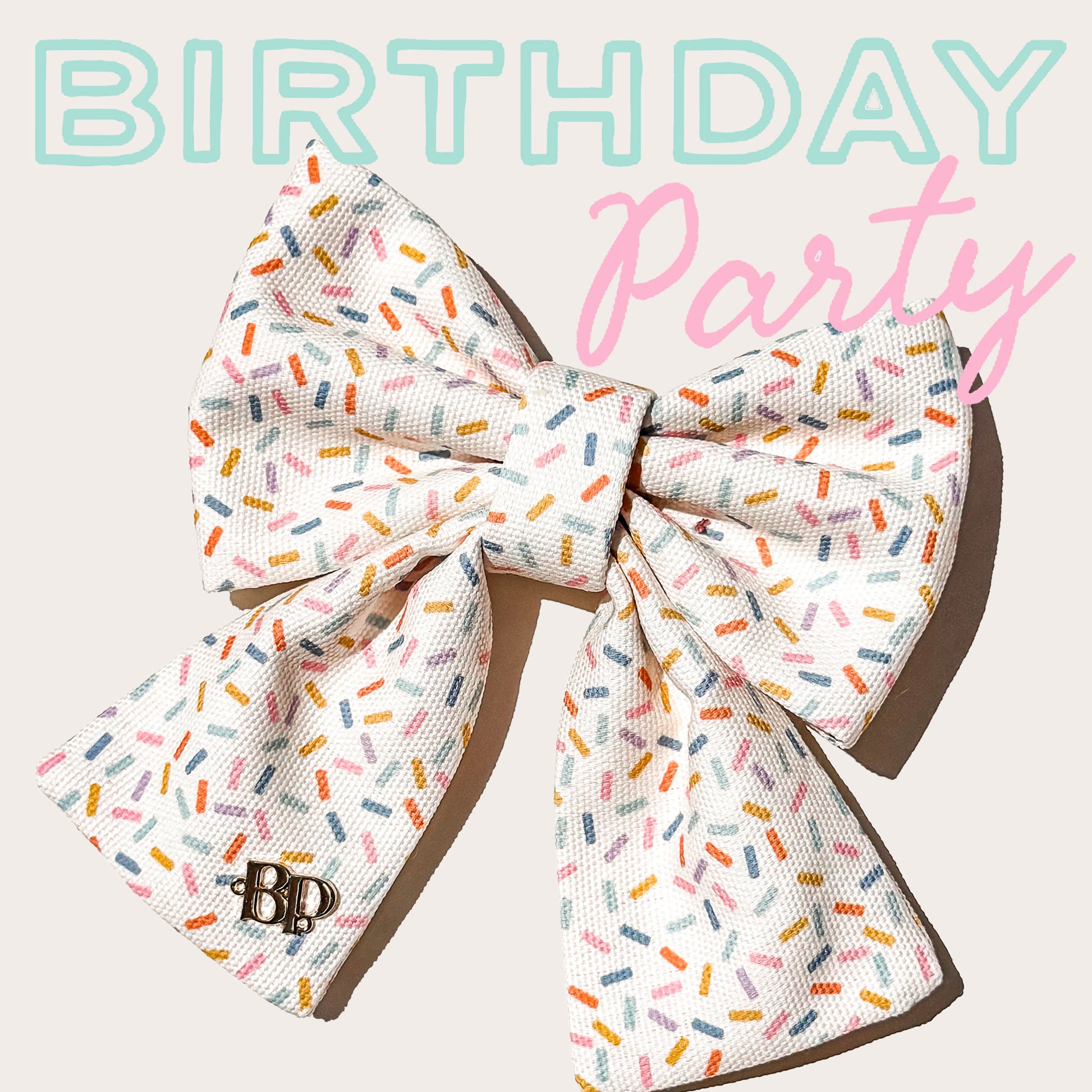 A large pet bow with a white base and a colorful sprinkle pattern, featuring a small 'BP' monogram on one loop. The bow is displayed against a light beige background with 'BIRTHDAY Party' text overlay in light blue and pink.