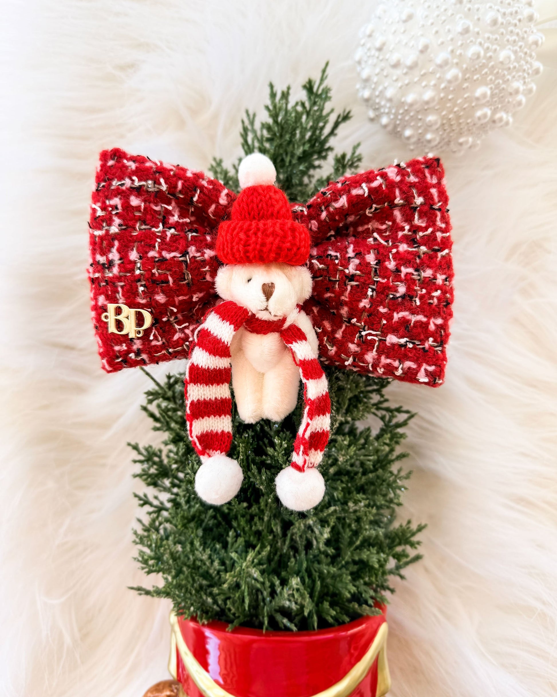 A festive red tweed Christmas Pet Bow Tie featuring a small white teddy bear wearing a red knit hat and striped red-and-white scarf, mounted on a green artificial tree with a large in a red pot at the base.