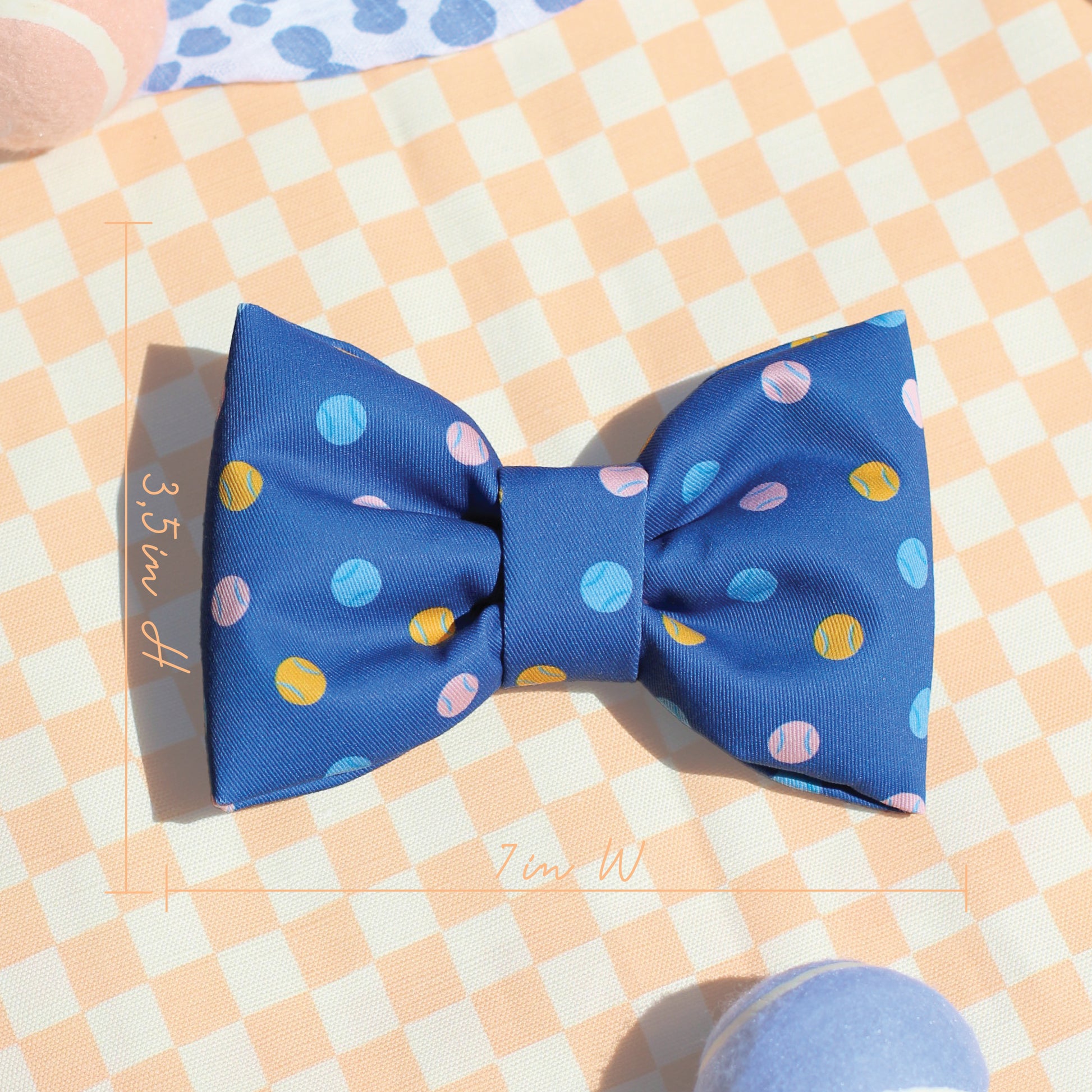 Blue bow tie with colorful tennis balls on a dog bow tie on a checkered fabric background for Bop Pop Pets all cotton, puffy bow ties for fashion, trendy dogs cats 